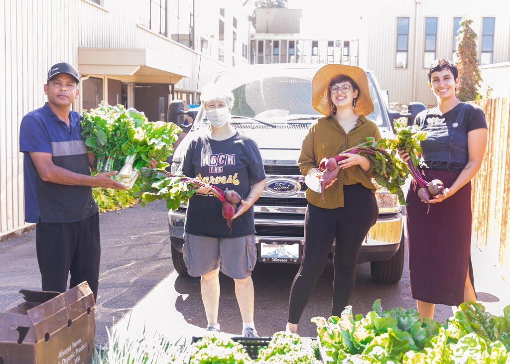 Four people standing in front of a truck, holding different vegetables -- beets and leafy greens.